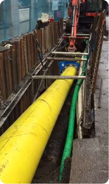A yellow plastic gas main being lowered into an excavation