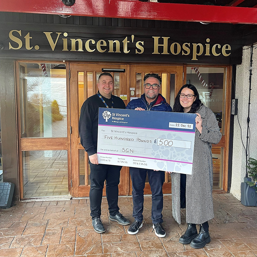 Three people holding a giant cheque outside St Vincent's Hospice