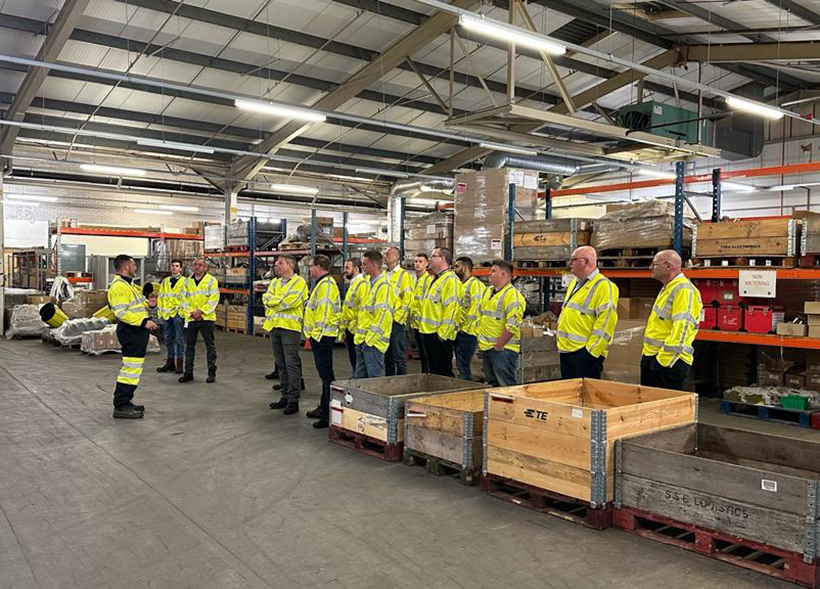 A group of new operatives to join SGN standing in our Stores Facility in Portsmouth. They are wearing safety jackets and listening to a talk from an existing member of staff.
