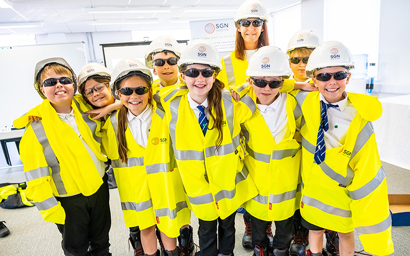 A group of children wearing yellow hi vis, hard hats and safety glasses
