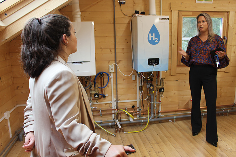 Two people talking indoors in front of three boilers in a demonstration home.