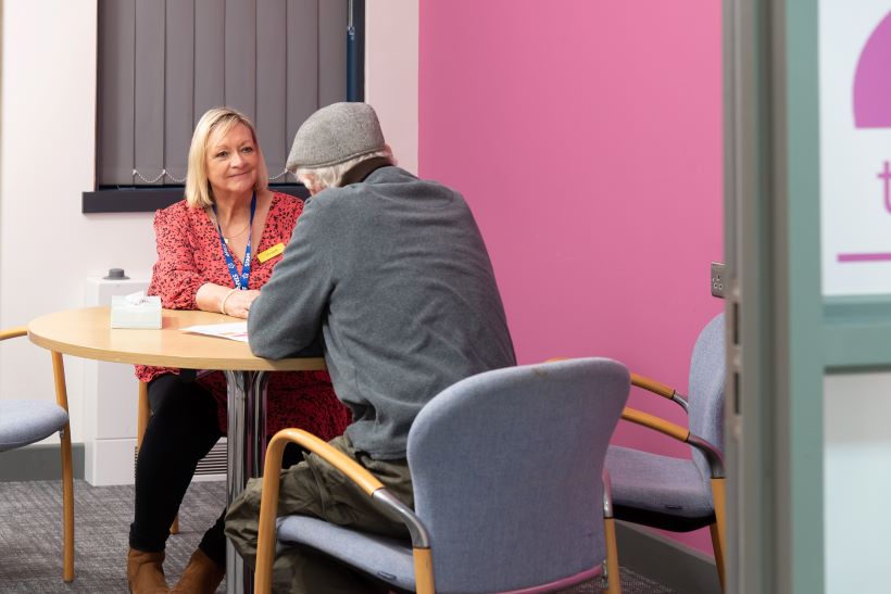 A Sage House service user is sitting at a table talking to one of the charity's support workers