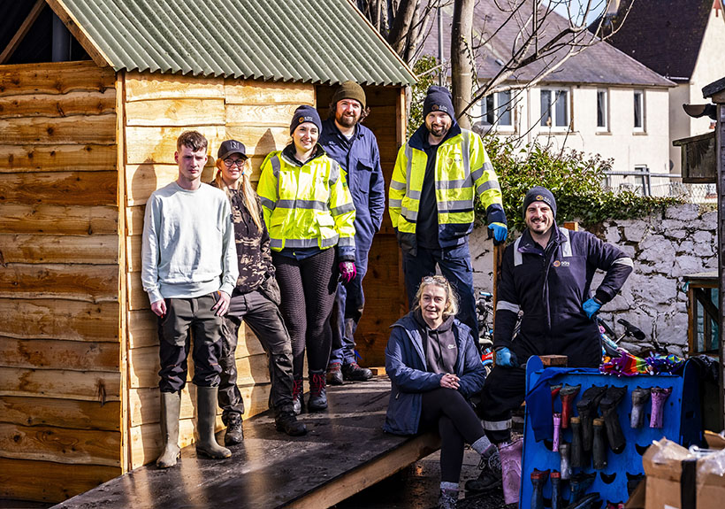 A group of people smiling standing in front of a shed on top of a ramp