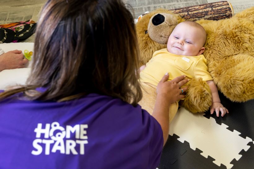 A smiling baby looks up at a Home Start worker