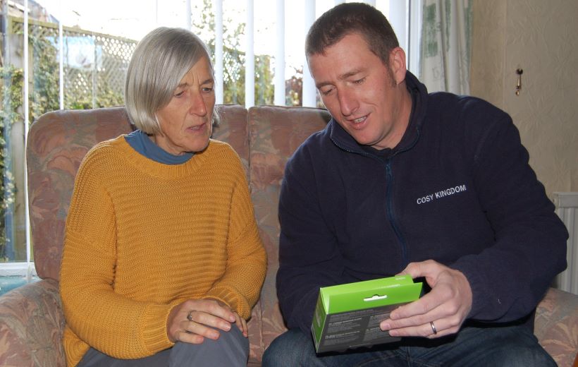 A Greener Kirkcaldy adviser is sitting on the sofa showing a CO alarm to a Fife resident