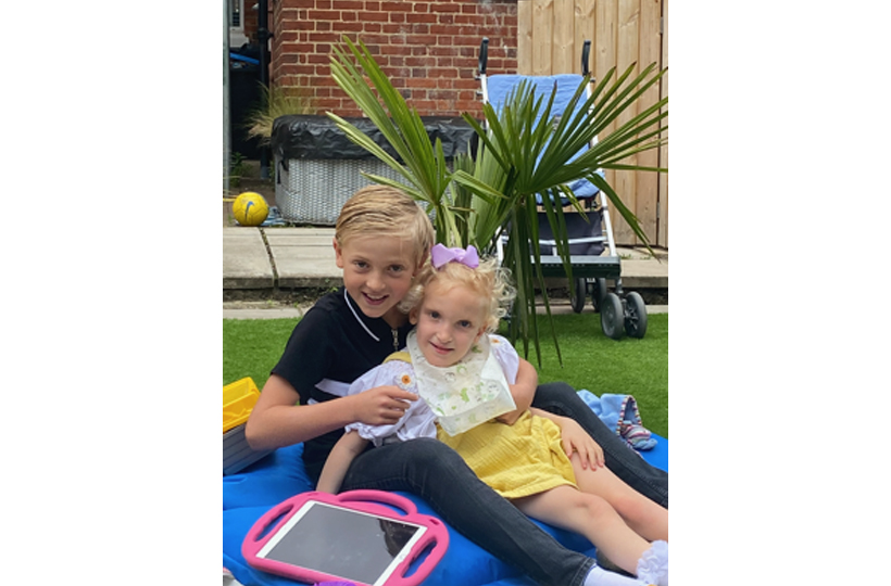 A young girl sitting on a young boy's lap on a bean bag in a garden