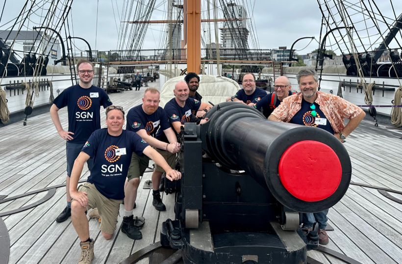 Eight volunteers in SGN tshirts surround a cannon on the deck of HMS Warrior