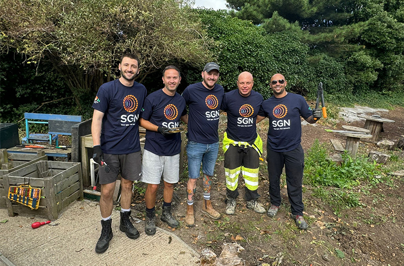 Our five SGN project managers wearing SGN t-shirts and holding tools in the cleared green space satisfied with a hard day’s work volunteering