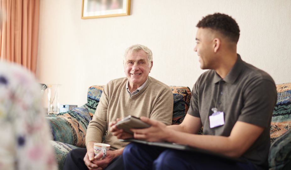 An older man is sitting on the sofa with an adviser