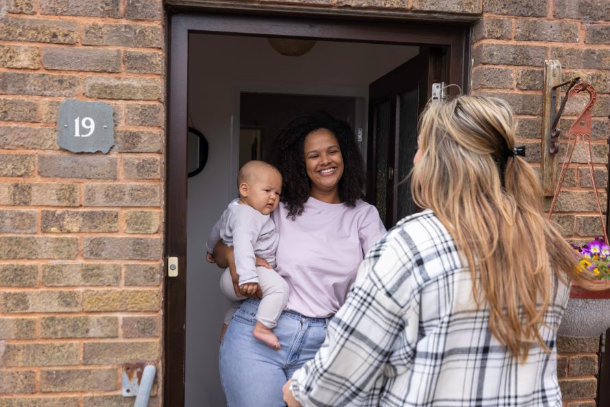 An Energy Action Scotland colleague is standing at a front door, talking to a mother who is holding her baby