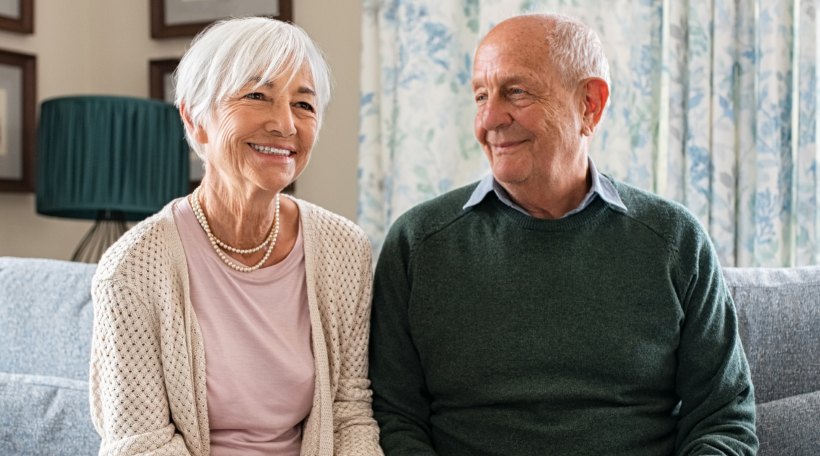 An older couple sit together on the sofa, smiling