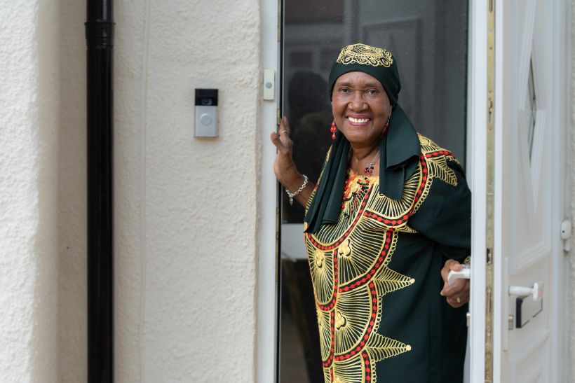 A smiling older lady is leaning out of her front door