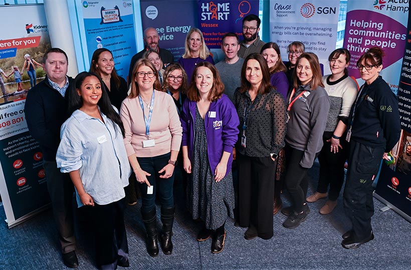 A large group of smiling people standing in front of stand-up banners representing the range of SGN's vulnerability partners in Dorset