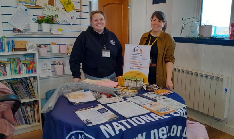 Two NEA Energy Advisors are standing behind a table of information at a baby bank in Harrogate