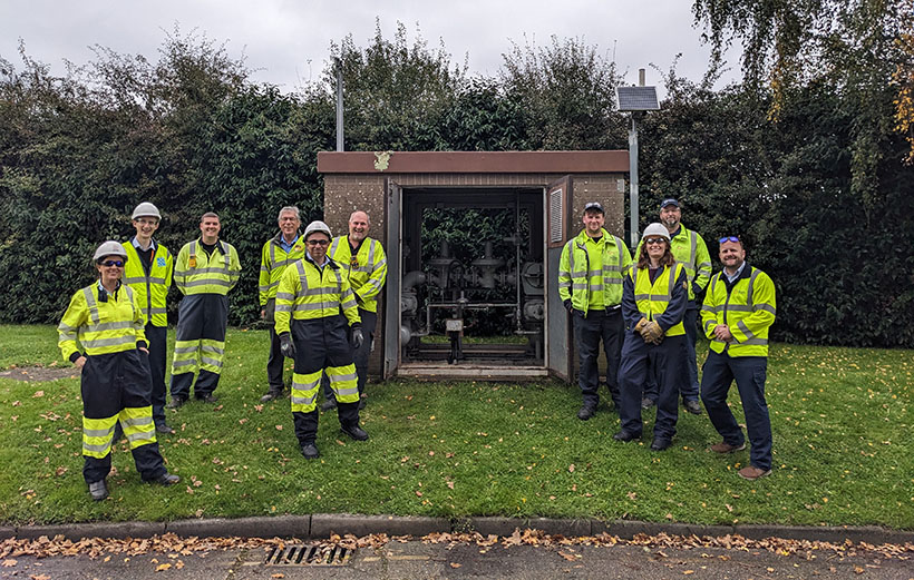 Gas engineers stand next to pressure reduction equipment. They are wearing protective clothing.
