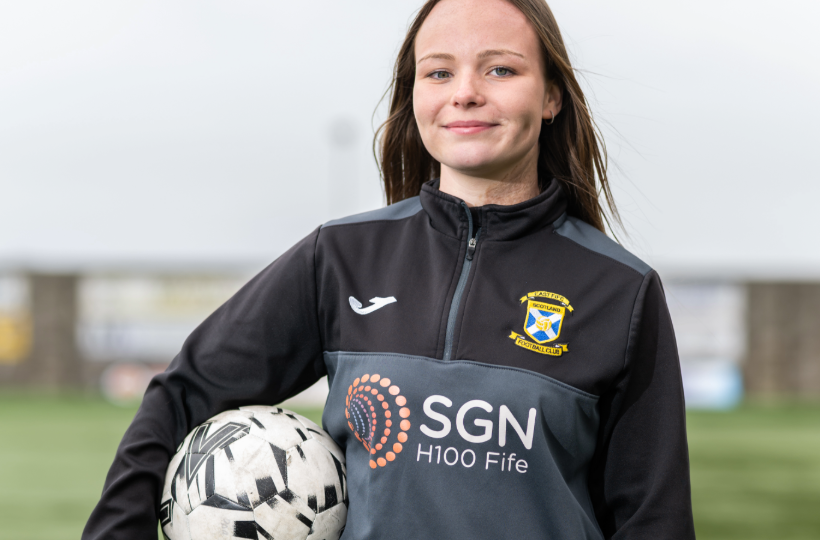 An older teenage girl wearing a football tracksuit and holding a football. She is smiling.