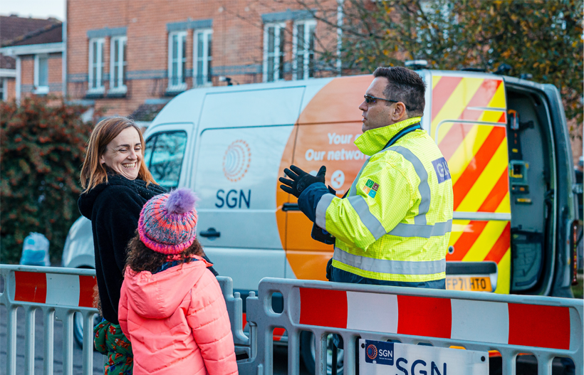 An engineer in PPE stood in front of an SGN speaking to a woman and her young daughter on the other side of our work barrier