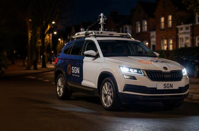 A white, SGN gas leak detection car driving down a residential street at nighttime.