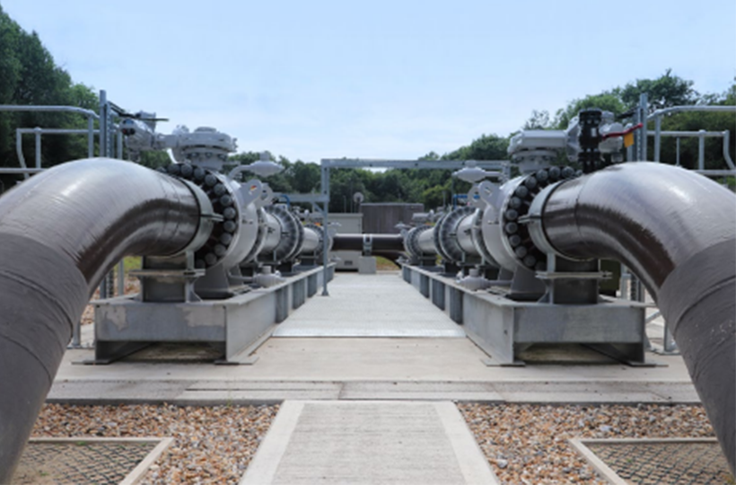 A pair of large grey gas pipes coming up from under the ground.
