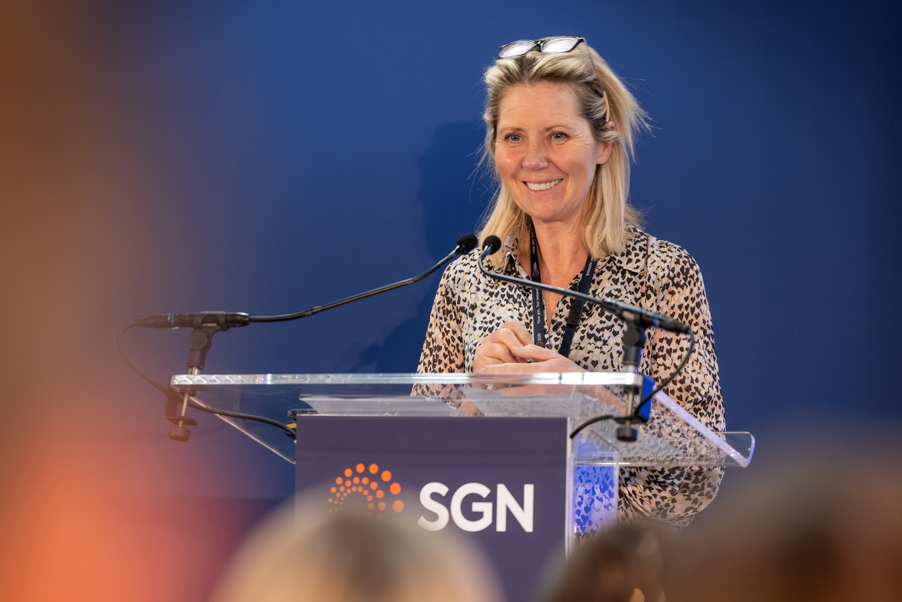 A smiling woman stood at a podium with an SGN logo