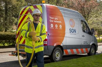 An SGN gas engineer walking away from his van carrying gas pipes