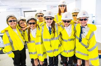 A group of children wearing yellow hi vis, hard hats and safety glasses