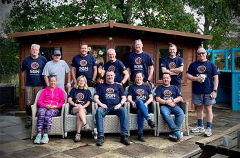 Twelve people in SGN t-shirts sat in front of a shed