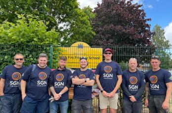 Seven people in SGN t-shirts in front of a sign for High Firs Primary School