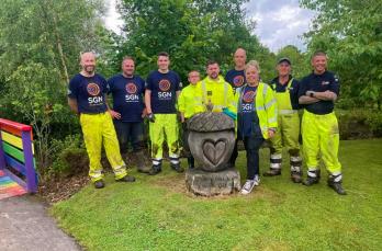 A group of engineers stood around a stone acorn monument in a freshly tidied garden