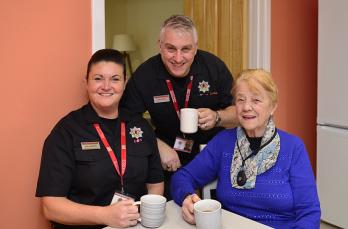 Two SFRS people sitting having a cup of tea with happy customer