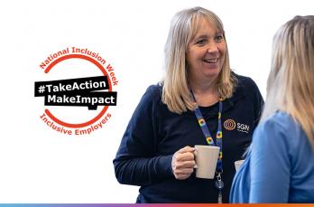 An mature woman in SGN PPE holding a mug while talking to someone, next to the National Inclusion Week logo