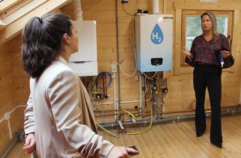 Two people talking indoors in front of three boilers in a demonstration home.