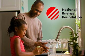 A Black man and his daughter stood in a kitchen washing their hands with soap and water from a running tap. Logo for National Energy Foundation is overlayed.