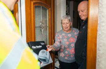 An elderly couple receive a fan heater in their doorway from someone in SGN PPE