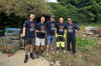 Our five SGN project managers wearing SGN t-shirts and holding tools in the cleared green space satisfied with a hard day’s work volunteering