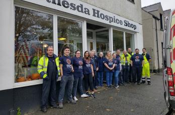 A large group of people outside a hospice shop in a street