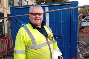 Head and shoulders image of man in his 50s with grey hair. He is facing the camera and wearing personal protective equipment