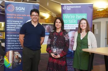 Three people smiling in front of pop up banners for SGN and Independent Age