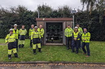 Gas engineers stand next to pressure reduction equipment. They are wearing protective clothing.