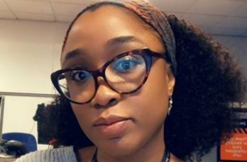 A Black woman with curly hair and glasses