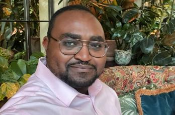 A Black man with glasses smiling at the camera