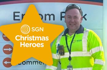 A smiling man in PPE in front of the entrance to our Epsom depot with a star that says 'SGN Christmas Heroes'