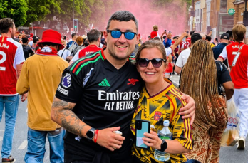 A man and woman in football shirts smiling at the camera surrounded by football fans