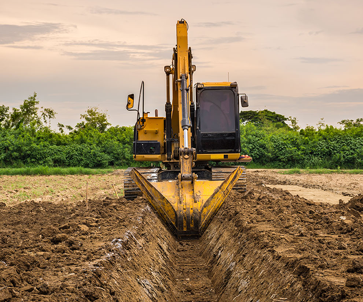 A yellow excavator digging a trench in a field